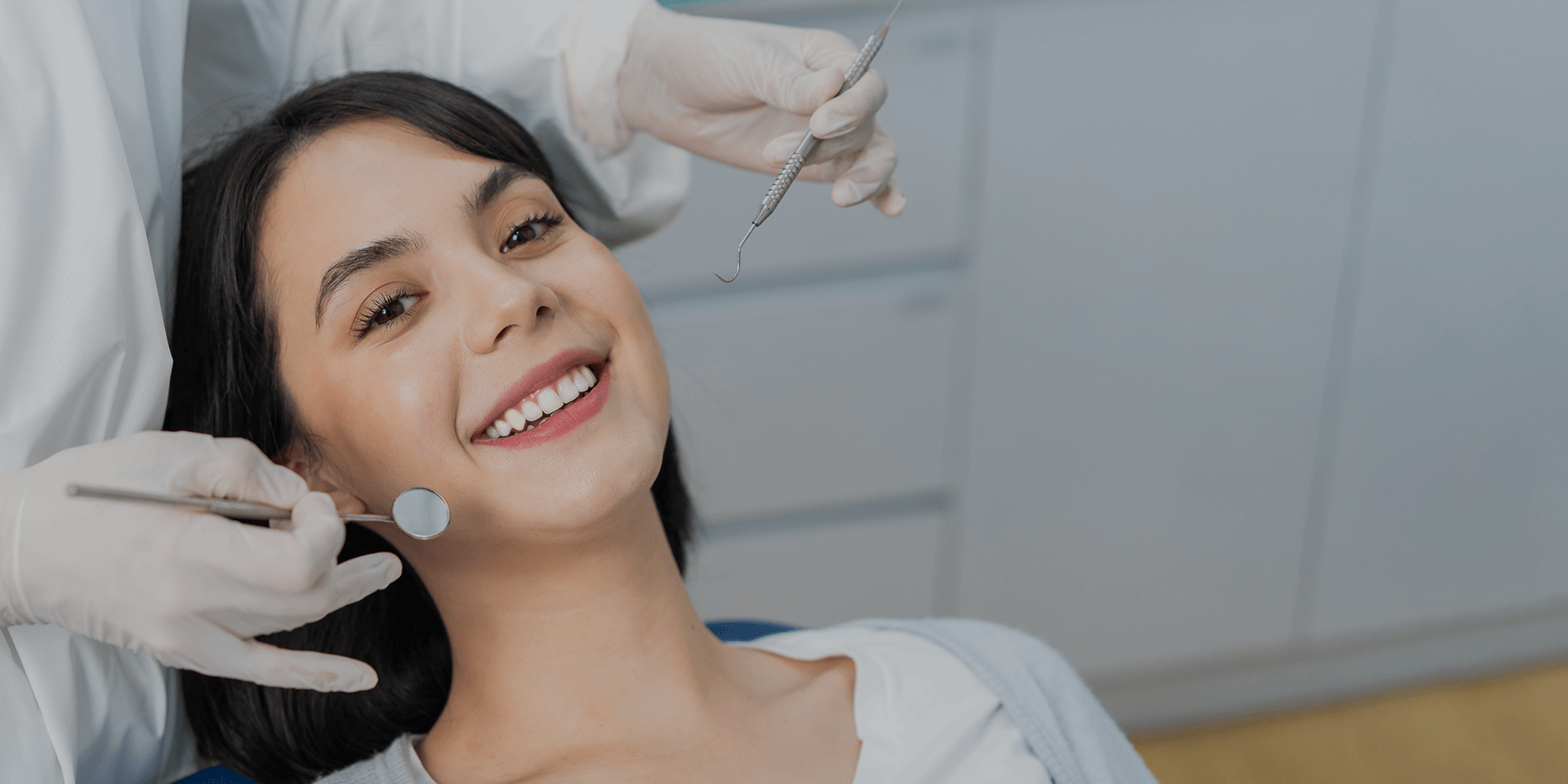 Smiling woman sitting in a dental chair during a check-up, with a dentist holding dental instruments.