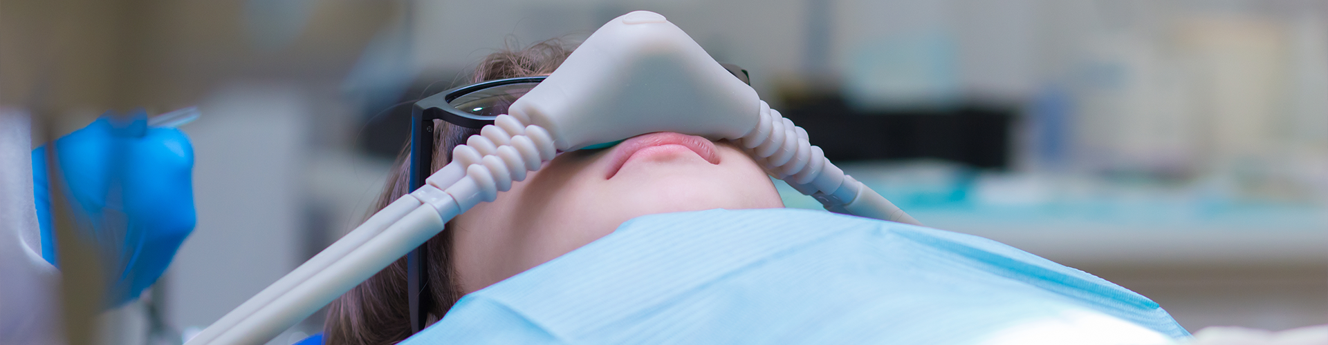 person on their back in dental chair with breathing mask over their nose.