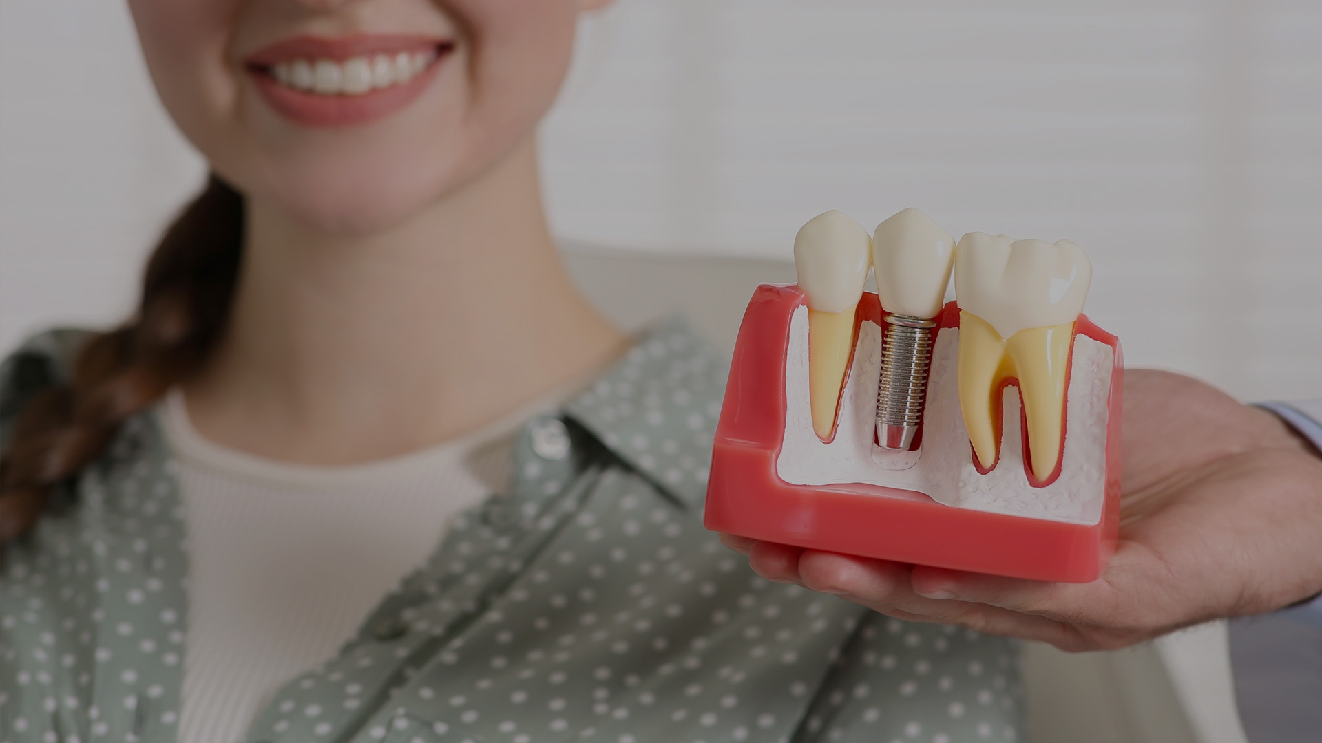 Woman holding a tooth model with a dental implant.